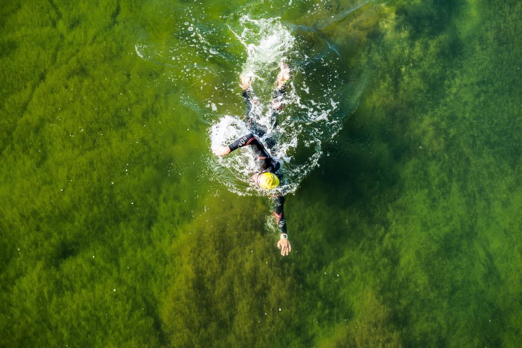 Photo of a person swimming in the sea. They are wearing a wetsuit, swim hat, and googles. 